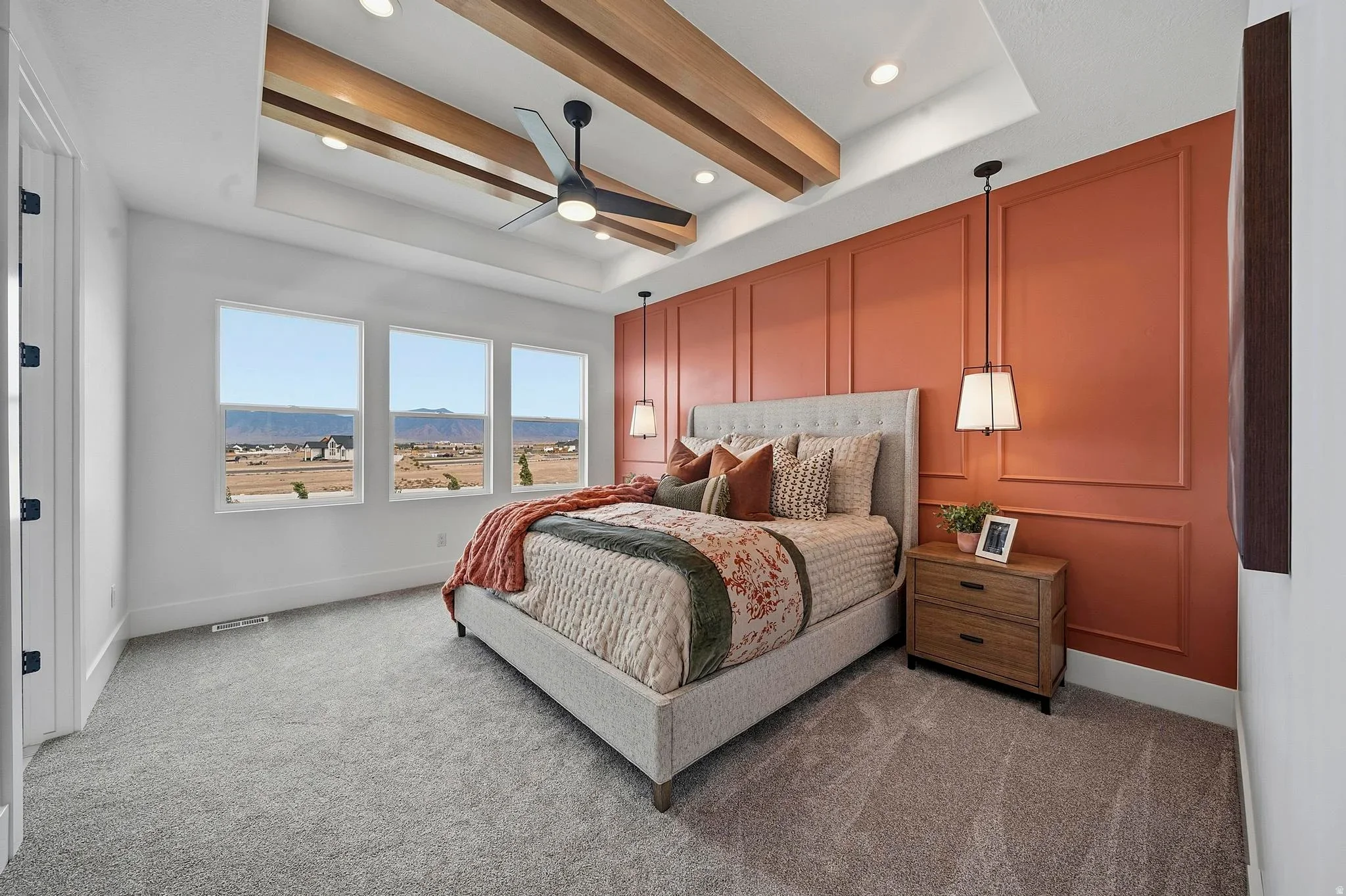 An Eagle Point Homes bedroom with a warm accent wall, ceiling beams, and mountain views